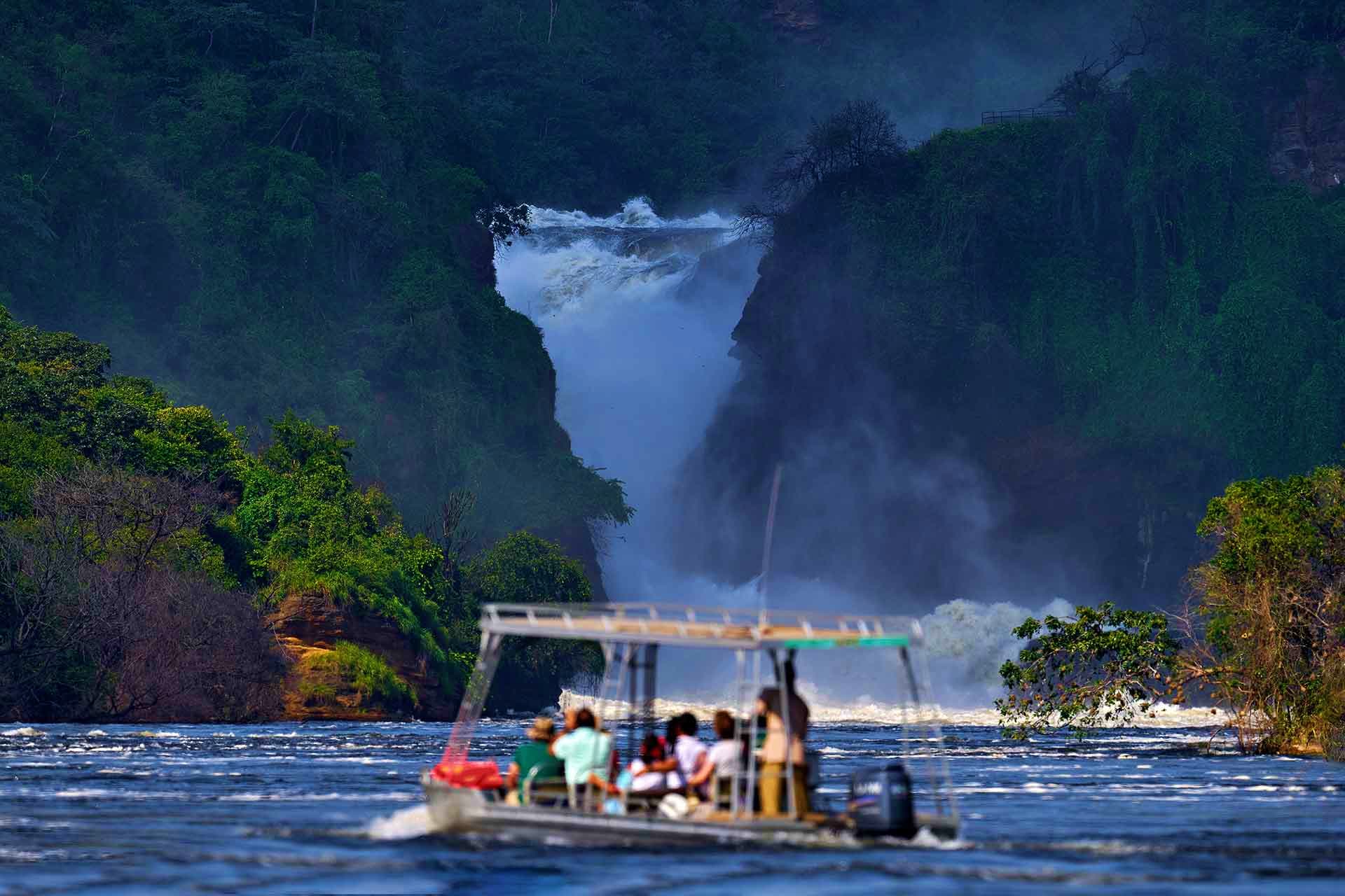 Kenya Visa Tourists in a boat on a river approaching Murchison Falls in Uganda, with dense forest and mist surrounding the powerful wate